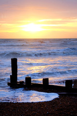 Naklejka na ściany i meble sun setting over a sea with waves breaking and a wooden sea break, Brighton, Uk