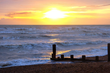 Fototapeta na wymiar sun setting over a sea with waves breaking and a wooden sea break, Brighton, Uk