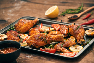 Grilled chicken drumstick and wings on baking tray over wooden table