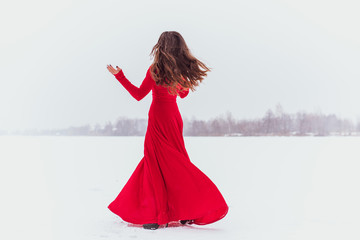 Hispanic woman dancing in silk dress at snowy day, artistic red flowing gown waving and fluttering...