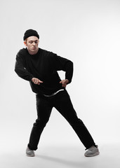 Young dancer dressed in black jeans, sweatshirt, hat and gray sneakers is dancing freestyle in the studio on the white background