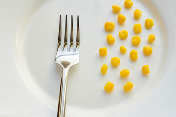 Top view of sweet corn on white plate and steel fork