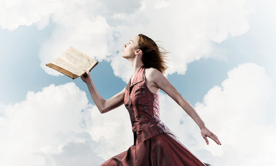 Girl against cloudy sky with opened book in palm as idea for kno - obrazy, fototapety, plakaty