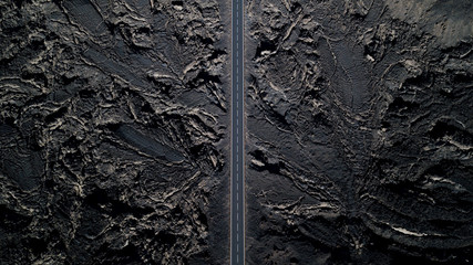 The road with white lines is surrounded by black volcanic lava. Sticking rocks. Dangerous adventure of incredible beauty. Top view, drone footage. Minimalistic landscape. 