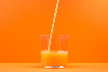 orange juice pouring in glass, isolated on orange background, copy space