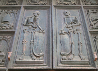 two skeletons carved in wood on the doors of an old church in Puglia