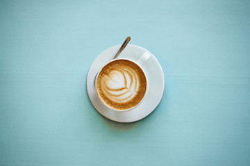 A cup with a traditional tasty and aromatic morning cappuccino on a blue background.