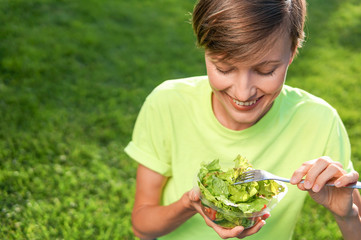 Beautiful caucasian woman eating salad over green natural background	