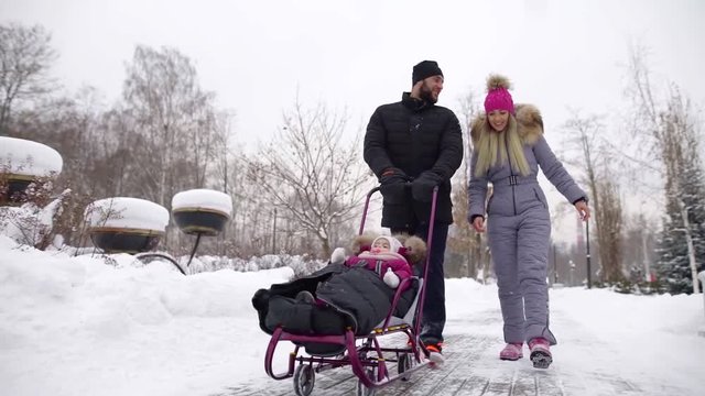 young European happy family walking in the winter snow-covered Park with a child to ride in the snow on a sled. Christmas vacation