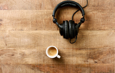 Black headphones and a cup of coffee on rustic wooden background. Top view, Copy space. 