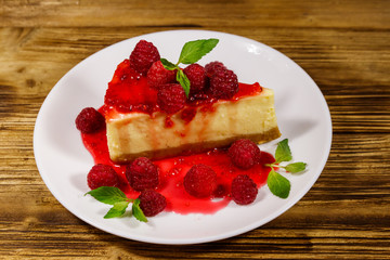 Piece of tasty New York cheesecake with raspberries and raspberry jam in a white plate on wooden table
