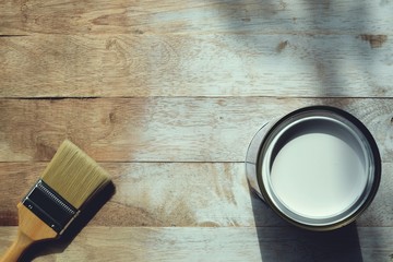 Painting brush and can of white oil color on wooden board background with blank space, top view color painting setup concept