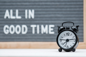 black alarm clock on the background of the text all in good time