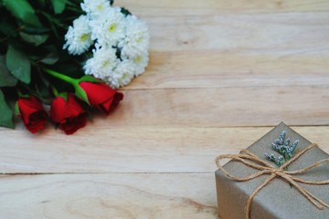 Eco friendly brown paper wrapped gift box present decorated with rose and other flowers on wooden background, valentine ornamental concept