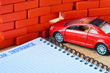 Miniature red car crashed in a brick wall and car insurance form
