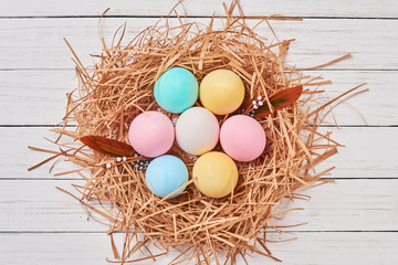 Colorful easter eggs in paper nest on a white background, top view. Easter decorations