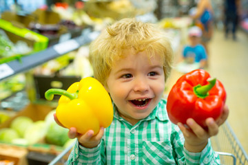 Fototapeta na wymiar Healthy lifestyle. Adorable little boy in supermarket shows his sincere happy emotions. Child plays with pepper at the store. Cute kid cheers in shopping cart in supermarket. Family shopping together