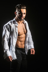 Fototapeta na wymiar Handsome man smiling. Attractive sports man takes off his shirt. Businessman with beautiful strong body. Passion lover. Young man with naked torso on black background looks into camera. Male clothes