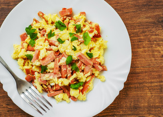 scrambled eggs with ham and cheese in white plate on wooden table background