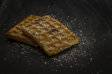 Delicious homemade belgian waffles on a black plate. Dessert with powdered sugar.