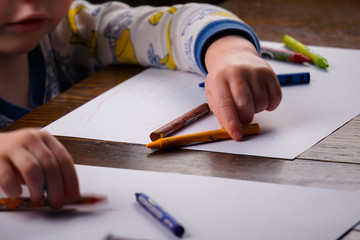 Toddler sitting at table coloring on white paper.