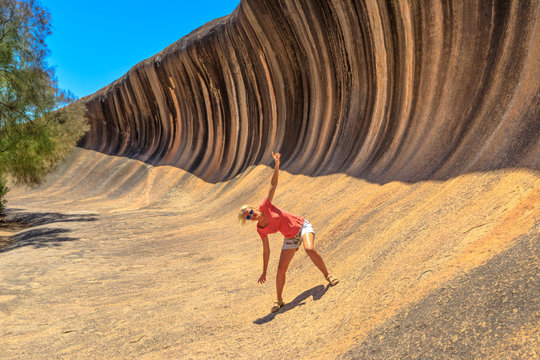 Blonde woman enjoying surfing on Wave Rock, a natural rock formation that is shaped like a tall breaking ocean wave, in Hyden, Western Australia. Happy funny girl in Australian outback. Copy space.