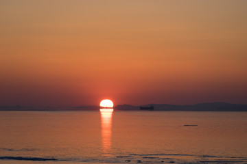 Seascape in orange and with bright sun on the horizon.