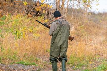 Fototapeta premium hunter with shotgun wearing waterproof uniform crossing river b