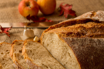   Pokorojony świeży chleb w kompozycji z jesiennymi liśćmi i czosnkiem.