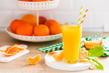 Tangerine orange juice in glass and fresh fruits with leaves on white wooden kitchen background closeup. Healthy and tasty refreshing summer beverage