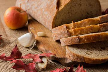   Pokorojony świeży chleb w kompozycji z jesiennymi liśćmi i czosnkiem. - obrazy, fototapety, plakaty