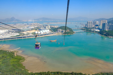 Ngong Ping Cable car with tourists over harbor, mountains and city background, to visit the Tian...