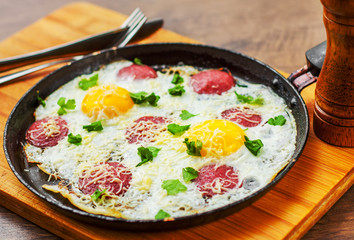 fried egg with ham sausage and cheese in a frying pan on wooden table background