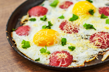 fried egg with ham sausage and cheese in a frying pan on wooden table background