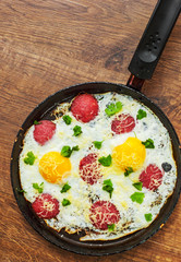 fried egg with ham sausage and cheese in a frying pan on wooden table background