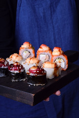 Sushi chef is holding a set of rolls on a black wooden board