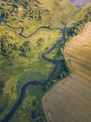 Aerial Photo the River Flowing Between Yellow and Green Agriculture Fields in Early Spring on Sunny Day