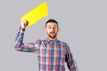 Young handsome man with facial hair holding blank paper speech bubble in hands with copy space for text. Bearded male, wearing hipster checkered shirt with empty message box. Isolated, background.