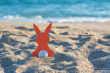 Creative easter concept photo of red paper bunny on the sand on the beach at sunset. Concept of Easter celebrations in tropical countries.