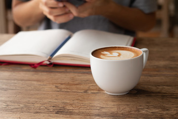 Woman checking her work on smart-phone blurred on background with warming drink, Late coffee in a cup in front-of on wooden table on-line working concept design