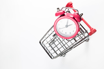 Pink alarm clock in the shopping trolley on a white background. Concept - time to buy. View from...