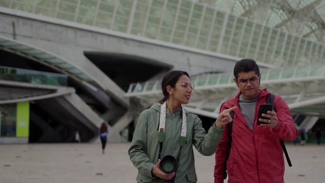 Excited hindu tourists walking on street and pointing at landmarks. Happy married couple with professional photo camera exploring new city. Travel concept