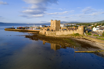 Fototapeta na wymiar Medieval Norman Castle in Carrickfergus near Belfast in sunrise light. Aerial view with marina, yachts, groyne, and far view of Belfast in the background.