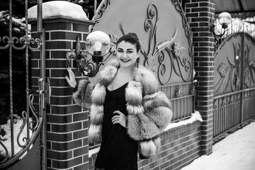Elegant arabic woman in fox fur coat and black dress outdoors, vintage style. Concept of femininity...