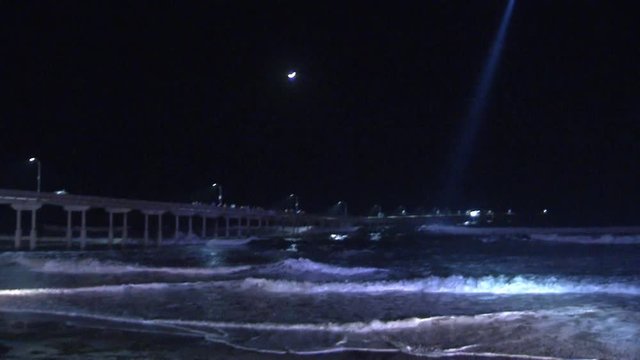 HELICOPTER SEARCHES THE OCEAN NEAR A PIER WITH ITS SPOTLIGHT