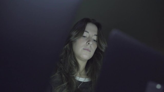Focused brunette girl using laptop in dark room. Low angle view of beautiful young woman working with laptop computer at night. Networking concept