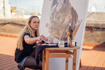 Young woman paint artist drawing at home roof. Picture of bulldog on big canvas. Outdoors art