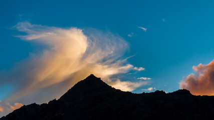 Clouds highlighted by sun above the mountain silhouette at sunset