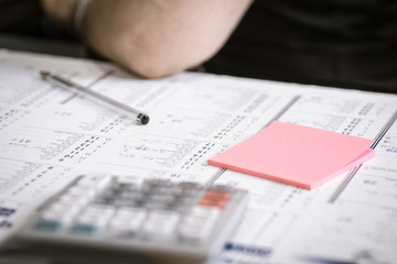Calendrier, post-it, calculatrice, stylo et coude sur bureau