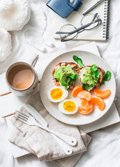 Cozy breakfast in bed still life - coffee, avocado sandwiches, boiled egg and tangerine on a light background, top view. Morning inspiration plan